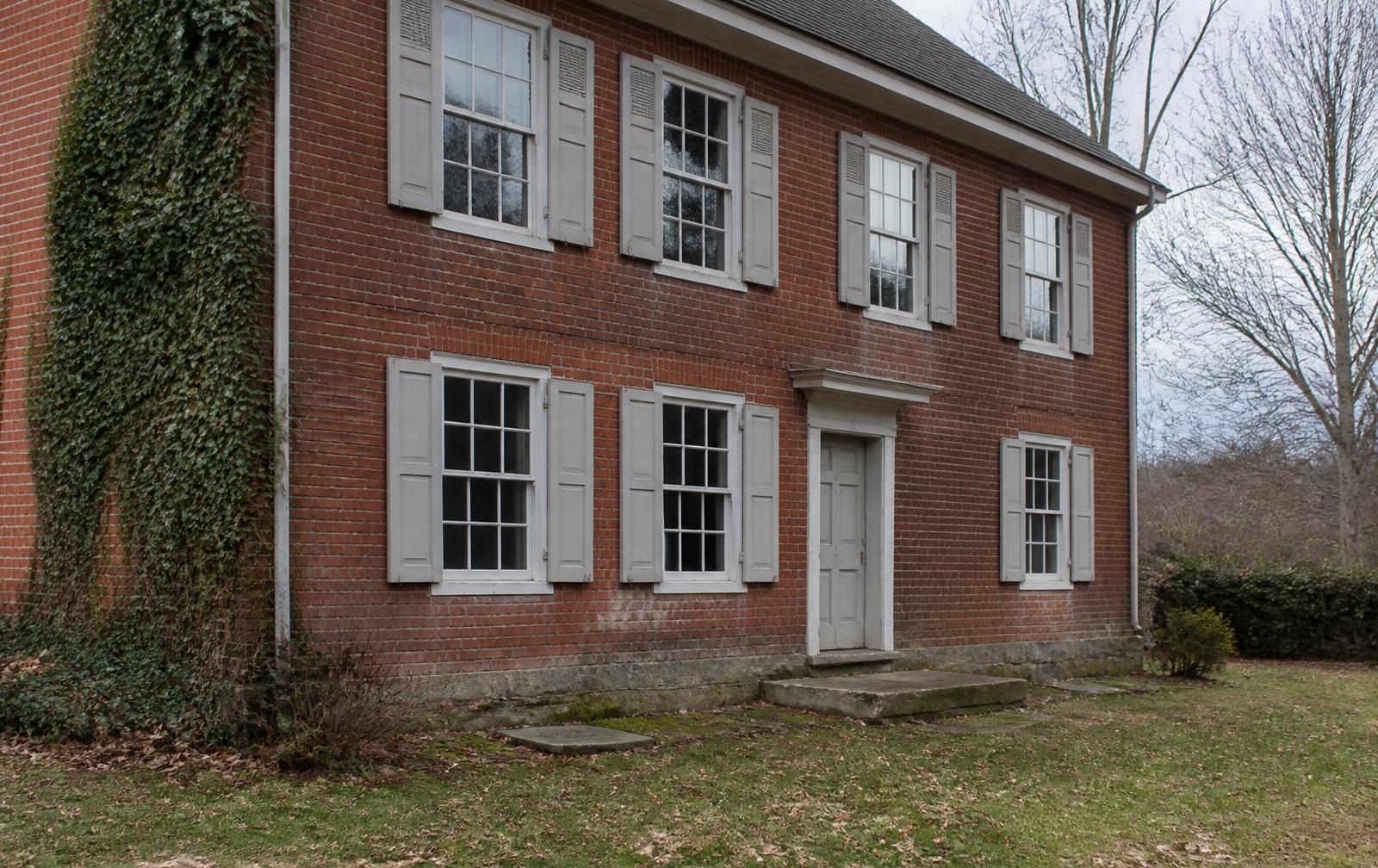 Brick facade of an 1820s Pennsylvania farmhouse with original shutters and stone step