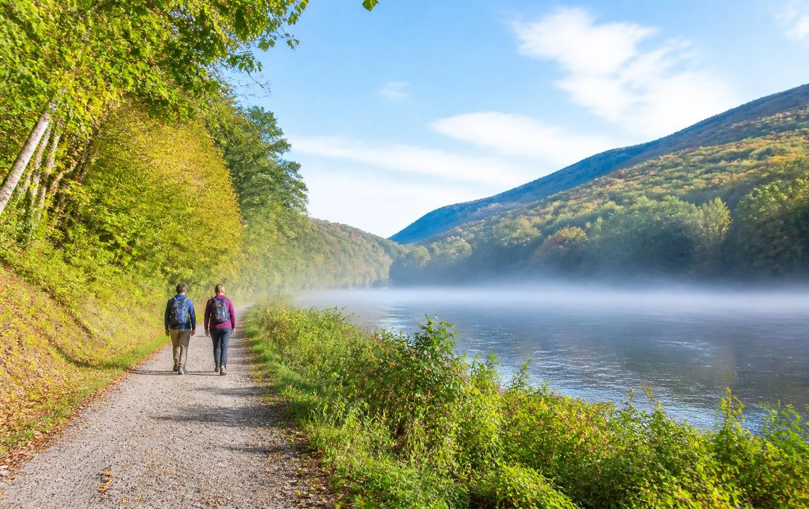 Two people walking a riverside rail trail on an early autumn morning